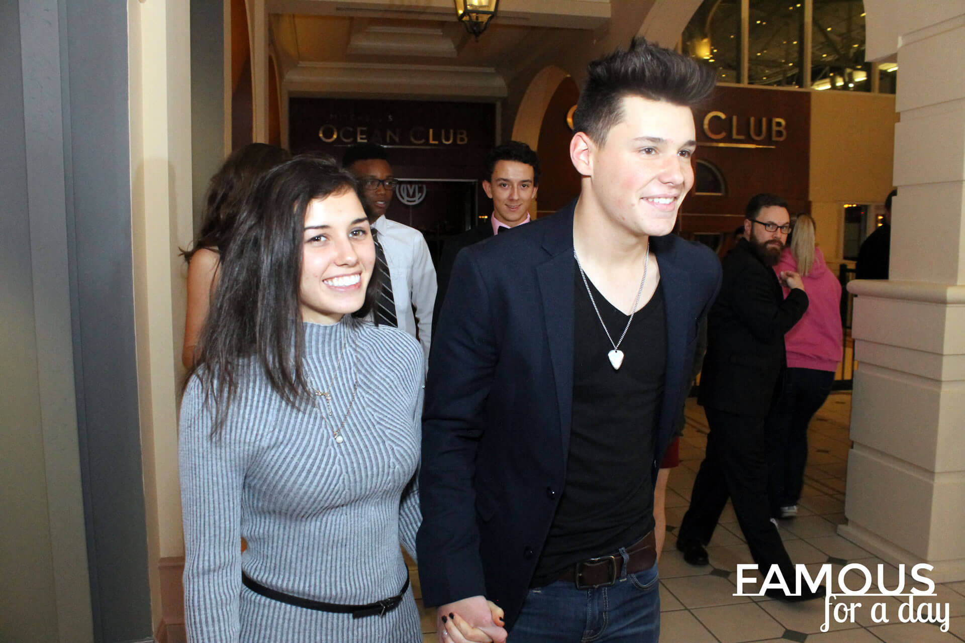 Young couple holding hands and smiling as they walk through a hotel entrance like celebrities